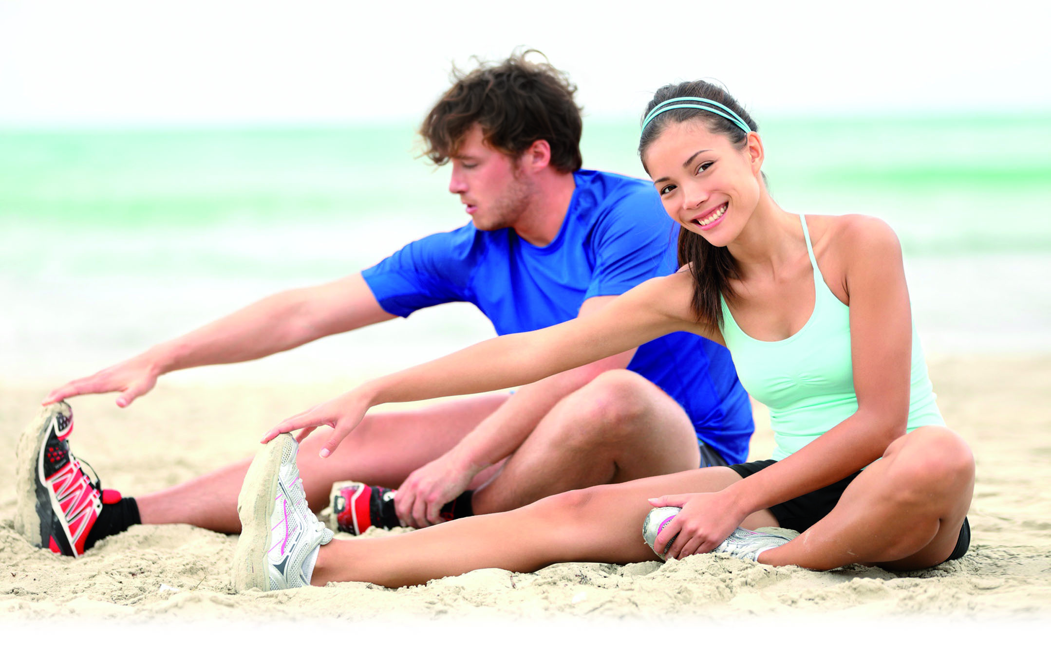 Ein junger Mann und eine junge Frau machen Dehn Übungen am Strand 